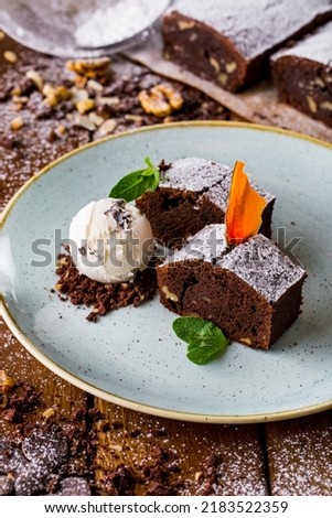 Chocolate cake with mint, lemon flower petals and a scoop of ice cream on a white plate. Vertical orientation