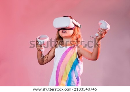 Video Gaming Concept. child girl playing with virtual reality goggles, VR headset, modern technology glasses  with neon light  on a colored background