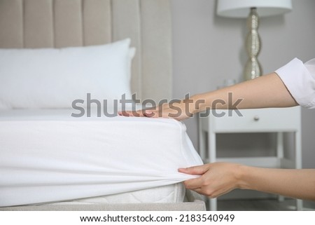 Woman putting white fitted sheet over mattress on bed indoors, closeup Royalty-Free Stock Photo #2183540949