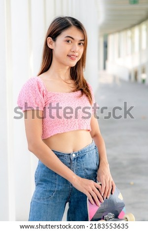 Portrait of beautiful asian woman holding skateboard in her hands standing outside befor playing in skate park.