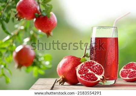 Pomegranate juice with fresh fruits on wooden table with pomegranate plant background. Royalty-Free Stock Photo #2183554291