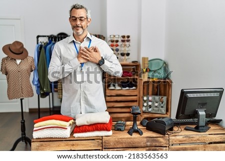 Middle age hispanic man working as manager at retail boutique smiling with hands on chest with closed eyes and grateful gesture on face. health concept. 