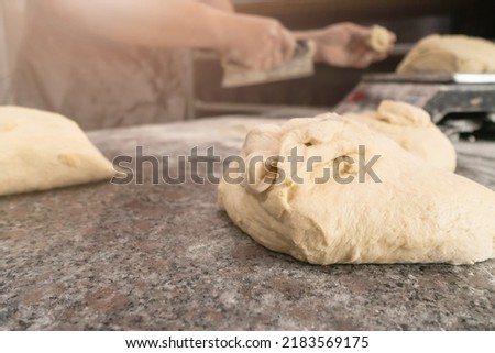 Close-up of elastic raw dough on a table sprinkled with flour, in the background a man cook weighs the dough by grams on a scale. Concept of baking, bakery