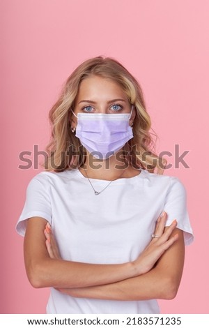 A young attractive woman in a white casual t-shirt wears a protective face mask. Protection against flu and cold diseases during a pandemic. Pink isolated background