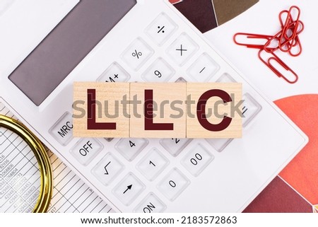 Flat lay, top view of office desk. Workplace with white calculator, magnifying glass, red paper clips and wooden cubes with text LLC Limited Liability Company