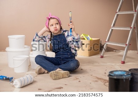A sad tired girl props elbow on the paint cans sighs lets the air out of mouth with an expression of lack of strength, holds in hand a paintbrush soiled with the brown color of the walls.