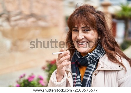 Middle age woman smiling confident smoking cigarette at street