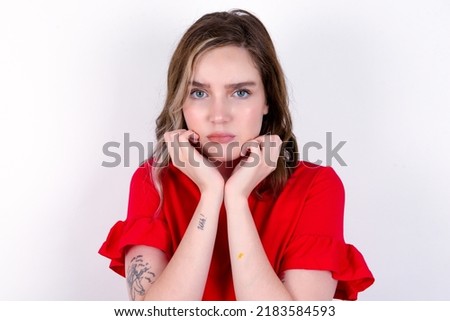 Portrait of sad young caucasian woman wearing red T-shirt over white background hands face
