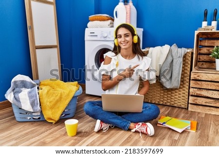 Young hispanic woman studying while waiting for laundry cheerful with a smile on face pointing with hand and finger up to the side with happy and natural expression 