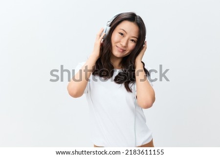 Dreaming happy cute Asian young female in white basic t-shirt touch headphones looks aside posing isolated on over white studio background. The best offer for ad. Favorite Music App Ad concept