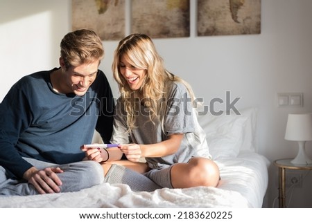 Happy young couple looking at pregnancy test on bed