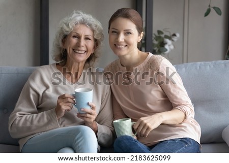 Portrait of happy old Caucasian 60s mother and grownup daughter relax on couch on family weekend enjoy warm coffee or tea in cup mug. Smiling mature mom and adult woman child rest together at home. Royalty-Free Stock Photo #2183625099