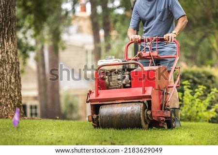 Man using gas powered aerating machine to aerate residential grass yard. Groundskeeper using turf aeration equipment for lawn maintenance. Royalty-Free Stock Photo #2183629049