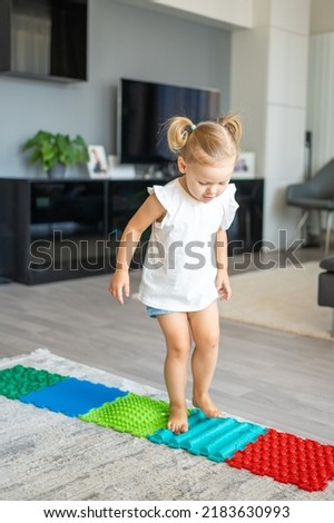 Little girl walks on a massage mat. Toddler baby foot massage mat. Exercises for legs orthopedic massage carpet. High quality photo