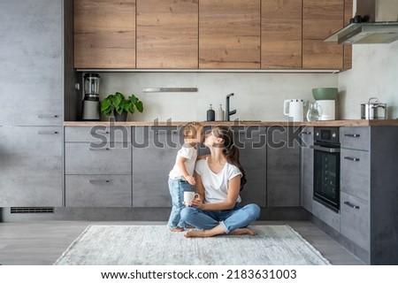 Little girl and happy mother with a cup of milk have a fun at home kitchen . High quality photo