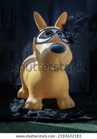 Yellow rubber dog doll wearing in black and white mysterious venetian mask with feathers design against dark background for copy space. Selective Focus.