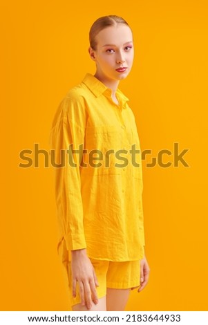Fashion and bright summer colours. Portrait of a pretty blonde girl posing in a bright yellow shirt and shorts. Yellow studio background. Summer fashion.  Royalty-Free Stock Photo #2183644933