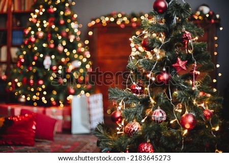 Evergreen Christmas Tree is Decorated with Red Toys and Luminous Garland. Yellow Bokeh Garlands in Background. Cozy Home Christmas Interior