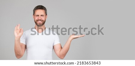 Happy guy show open hand making OK ring gesture grey background copy space, presenting product. Man face portrait, banner with copy space.
