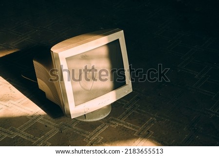 An old dusty computer monitor stands in an abandoned room on a dirty floor, the sun from the window illuminates this device, the atmosphere of sadness and abandonment