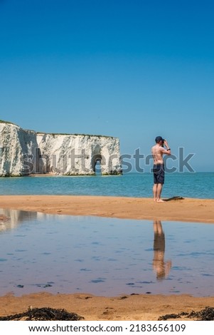 A topless man taking photography on the sandy beach at Kingsgate Bay in the seaside town of Broadstairs, east Kent, England, Kingsgate Bay Sea Arch in the background