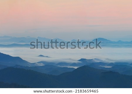A bird's eye view of the high peaks interspersed in layers amid the white mist and the pale pink sky of golden light in the morning.