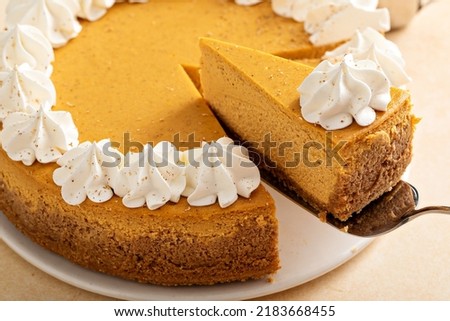 Pumpkin cheesecake with fall spices topped with whipped cream, dessert for Thanksgiving, whole cake with two slices cut