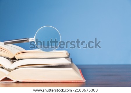 open book with magnifying glass on wooden desk in information library of school or university, concept for education,reading , study, copy space and blue background. Royalty-Free Stock Photo #2183675303