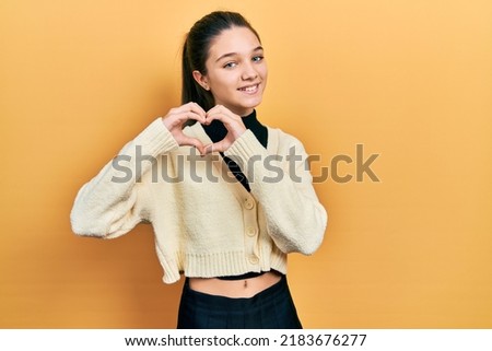 Young brunette girl wearing casual yellow jacket smiling in love doing heart symbol shape with hands. romantic concept.  Royalty-Free Stock Photo #2183676277