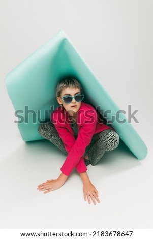 Portrait of young girl in bright jacket and vintage pants posing with paper piece isolated over grey studio background. Concept of retro fashion, art photography, style, beauty