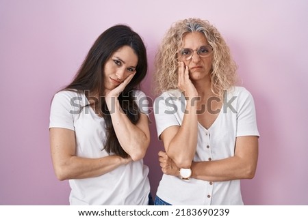 Mother and daughter standing together over pink background thinking looking tired and bored with depression problems with crossed arms. 