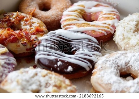 Picture of assorted donuts in a box with chocolate frosted, powdered, and sprinkles donuts.