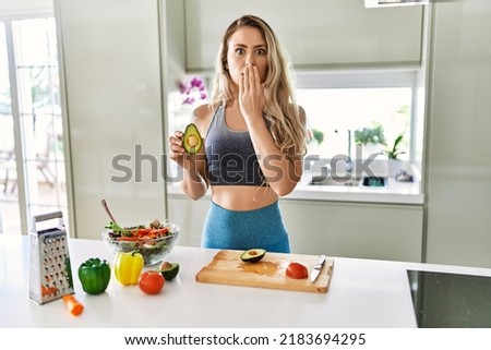 Young caucasian fitness woman wearing sportswear preparing healthy salad at the kitchen covering mouth with hand, shocked and afraid for mistake. surprised expression  Royalty-Free Stock Photo #2183694295