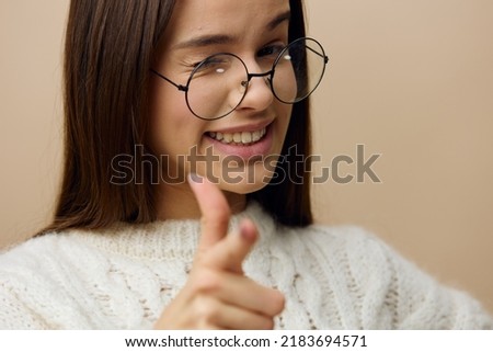 a pretty woman stands on a light background in a white sweater and glasses, animatedly pointing with her fingers and winking and sticking out her tongue a little, thereby showing her approval
