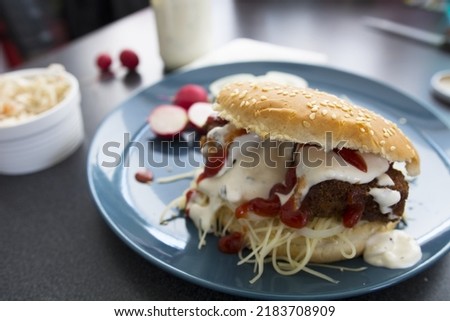 Fish burger with tartar sauce and ketchup on a blue plate.