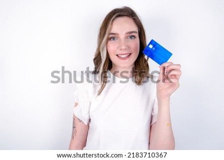 Photo of happy cheerful smiling positive young caucasian woman wearing white T-shirt over white background recommend credit card