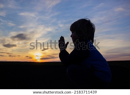 silhouette of a boy, folded his hands in prayer, turning to God against backdrop of a picturesque sunset. Children against war. child asks for peace for his homeland Ukraine. Stop Russian aggression