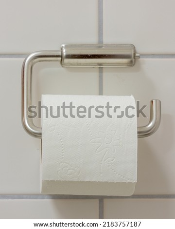 Toilet paper in holder, bathroom tissue,  white tiled wall Royalty-Free Stock Photo #2183757187