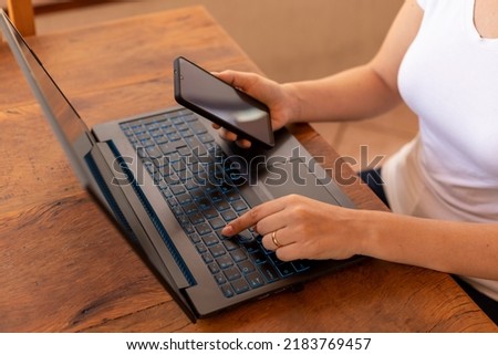 woman with cellphone in hand and typing on laptop. home Office Royalty-Free Stock Photo #2183769457