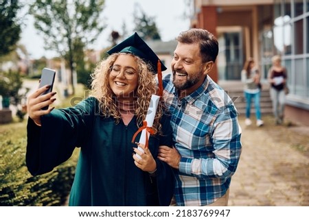 Happy university graduate and  her father having fun while taking selfie with smart phone.