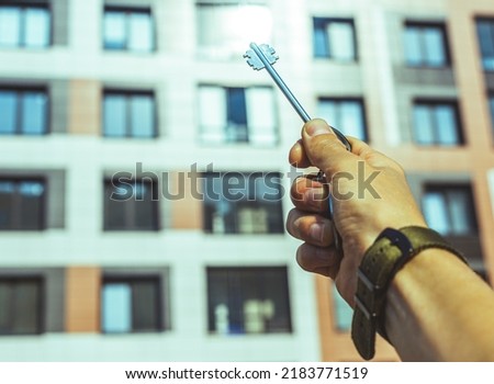 A man's hand holds the keys to a new house against the background of high-rise buildings close-up selective focus. A man holds the keys to a new apartment against the backdrop of high-rise buildings. 