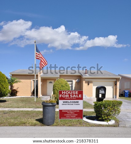 American Flag pole Real Estate for sale welcome open house sign on front yard lawn of suburban ranch style home with trash can on curb side residential neighborhood USA blue sky clouds