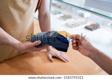 Cropped view of salesman holding payment terminal near african american customer in sweet shop