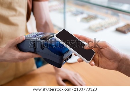 Cropped view of african american client paying with smartphone near seller in sweet shop