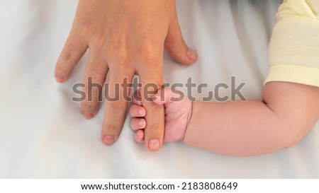 Hand of little baby and finger of adult on white sheet bed background with day light. Cute boy and chubby hands of a child. The age of 3 months learns to touch and grab.