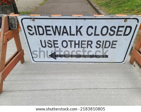 A sign indicating that the sidewalk is closed and to use the other side of the road.