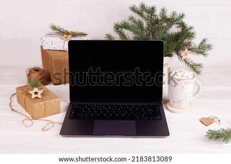 Laptop screen, cocoa mug with marshmallows, gift box, Christmas tree branches on a white wooden background. Shopping online for the Christmas holidays. Mock up