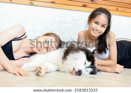 Beautiful asian girl and caucasian girl posing with a big friendly siberian husky dog at home.