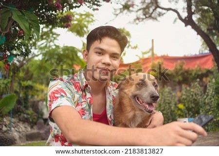 A portrait of a loving owner and his furry friend in a backyard garden. Dog is distracted by another silly dog.