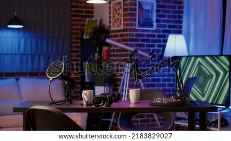 Empty vlogger desk with professional streaming equipment to broadcast live talk show on social media. Cozy ambient room with podcast station, microphone and headphones, sound production.